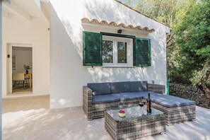 A wicker sofa and a glass coffee table with a bottle and glasses on it, positioned in front of a white building with green shutters. - Premium Pollensa Country Villa for 6 (Pollensa)