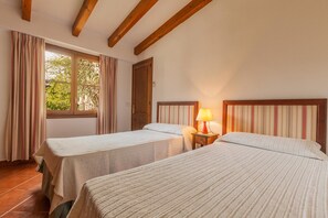 Ein Zimmer mit zwei Betten, einem Vorhangfenster, einer Holztür und einem Nachttisch mit Lampe.