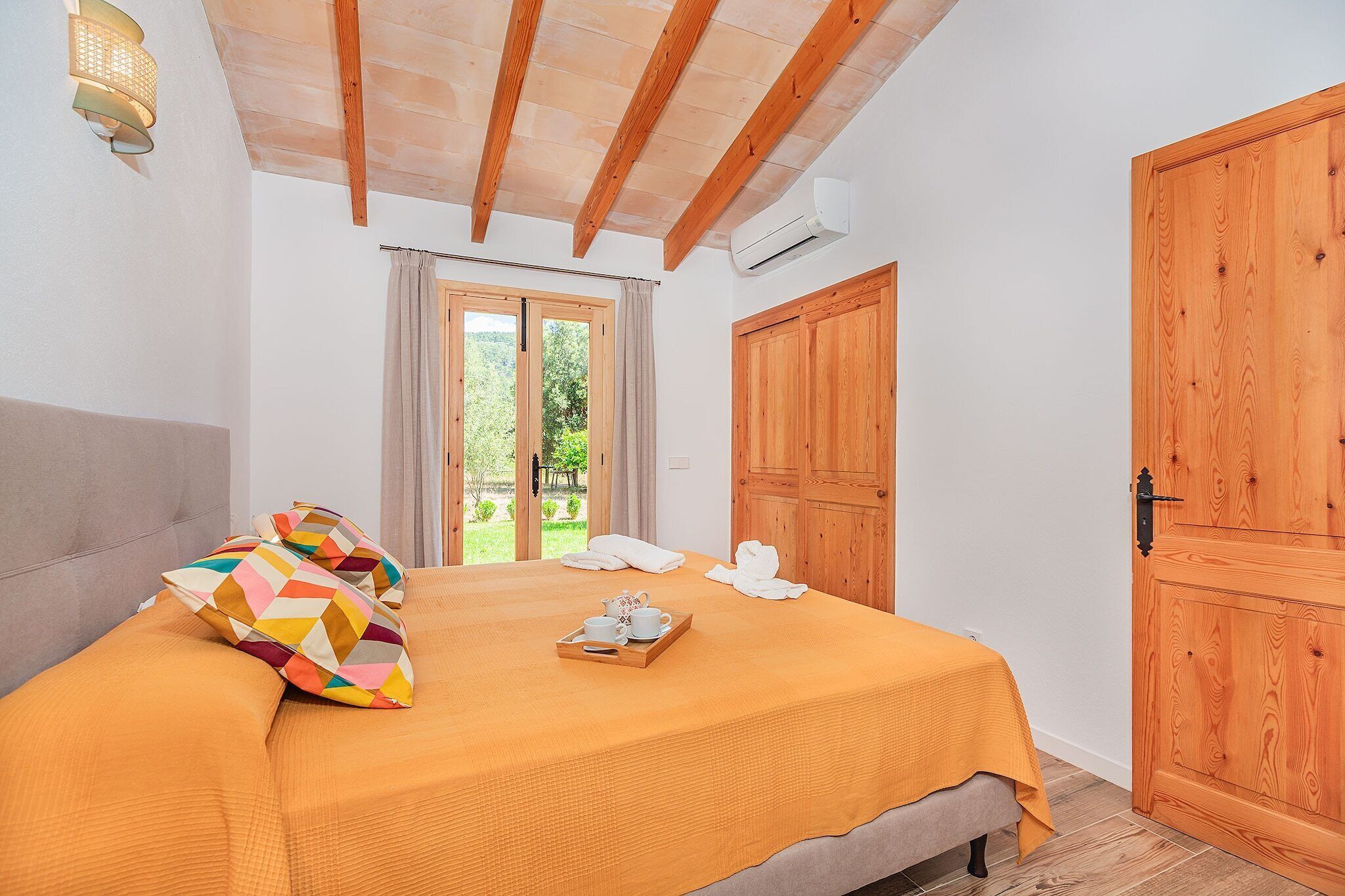 A bedroom with a bed, a wooden door, a window with curtains, and a wall-mounted light fixture.