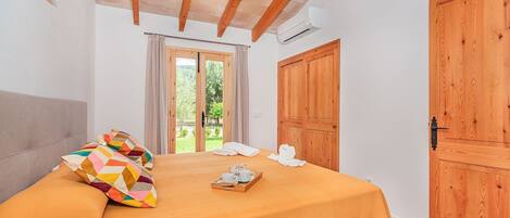 A bedroom with a bed, a wooden door, a window with curtains, and a wall-mounted light fixture.