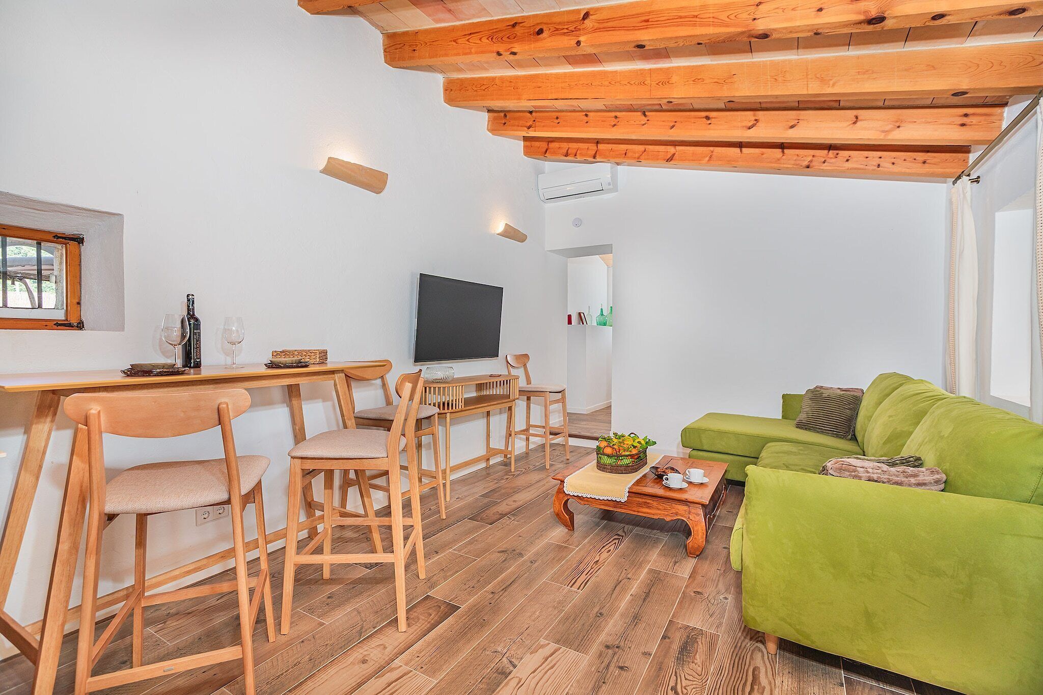 A living room with a wooden dining table, chairs, a green sofa, and a television.