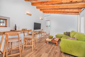 A living room with a wooden dining table, chairs, a green sofa, and a television. - Rural Majorcan Country Villa with Pool (Campanet)