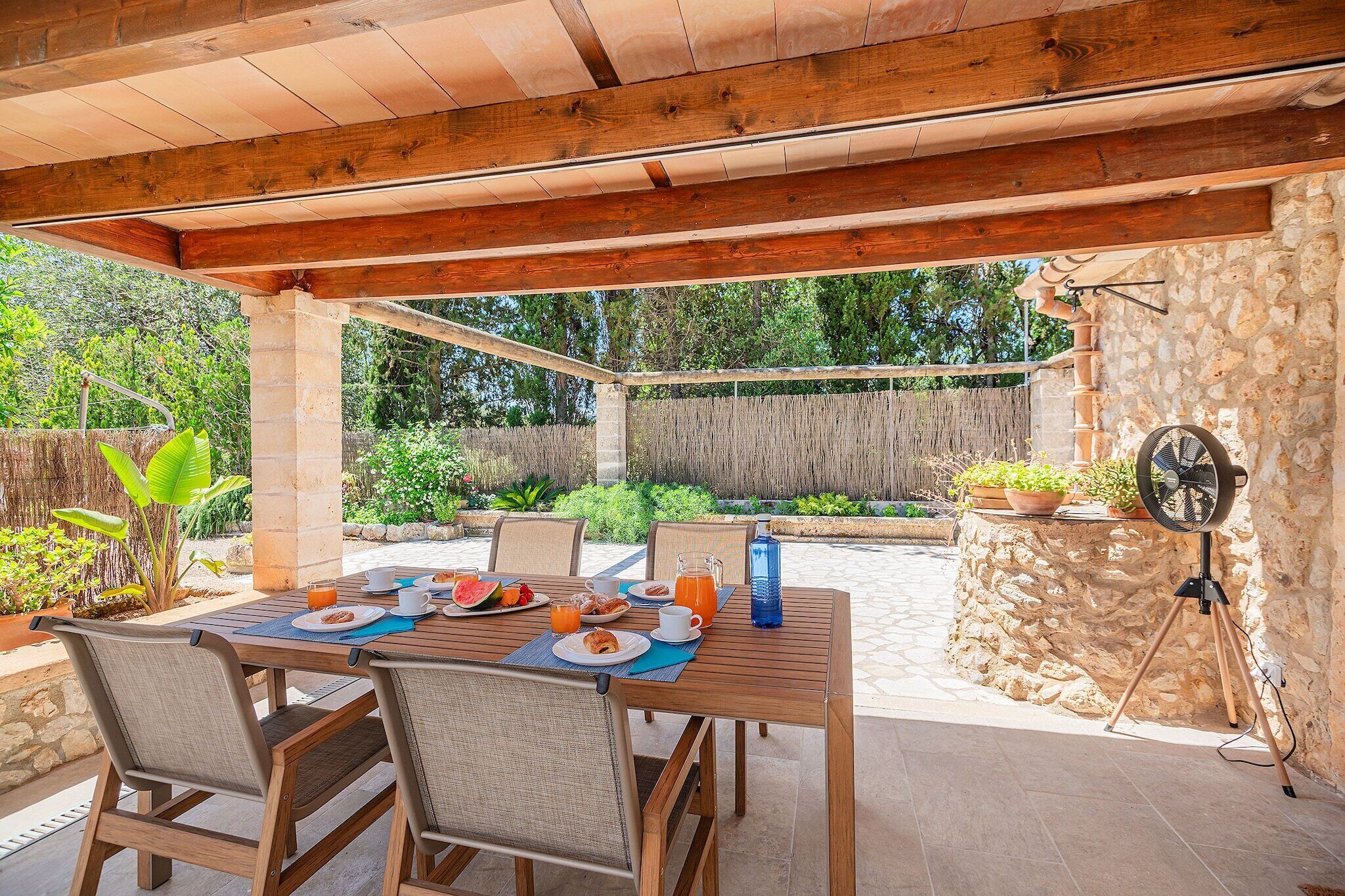 Une terrasse extérieure avec une table en bois mise pour le petit-déjeuner, entourée de murs en pierre et de verdure.