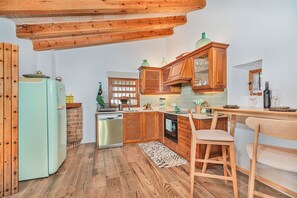Ett kök med träskåp, ett kylskåp, en diskho och en matplats med en stol och ett bord.