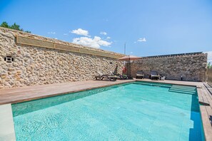 Una piscina con pared de piedra y cubierta de madera, rodeada de sillones de descanso.