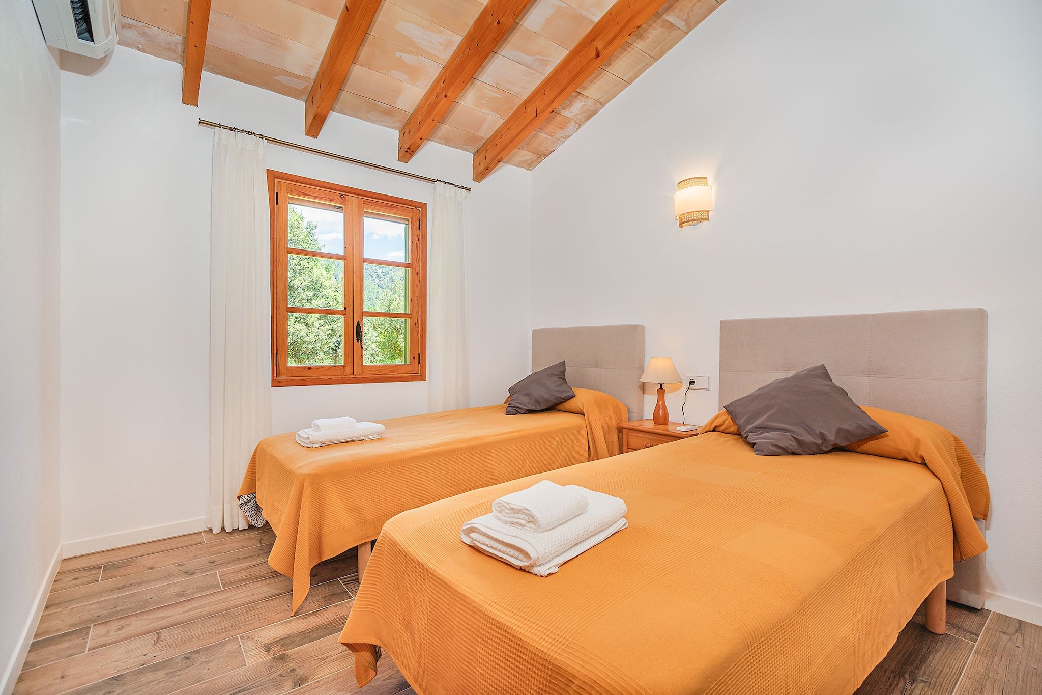 Ein Zimmer mit zwei Betten, einem Fenster mit Aussicht, einer Wandleuchte und einer Holzbalkendecke.