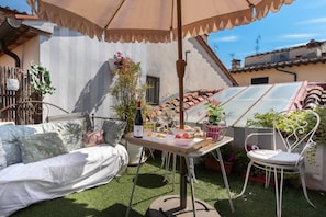 Um pátio externo com uma mesa posta para refeições, um sofá e uma cadeira.