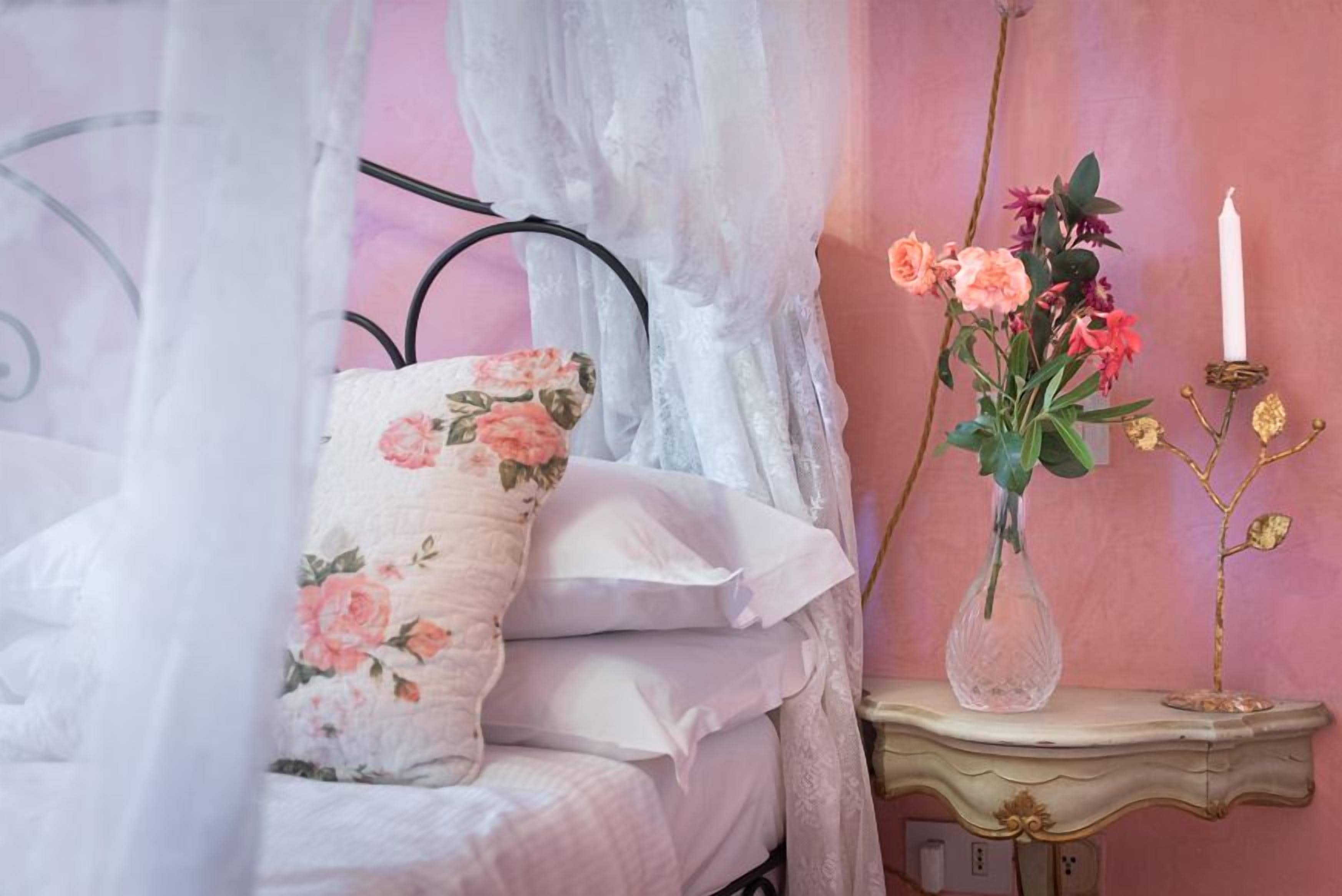 Une chambre à coucher avec un lit, une table de chevet, un vase de fleurs et une bougie.