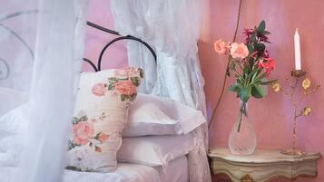 Ett sovrum med en säng, ett nattduksbord, en vas med blommor och ett ljus.