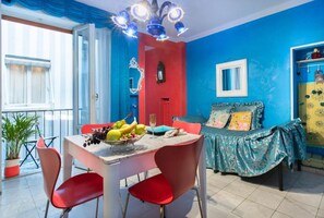 Quarto com mesa de jantar, cadeiras, cama com cobertura estampada e janela com cortinas.