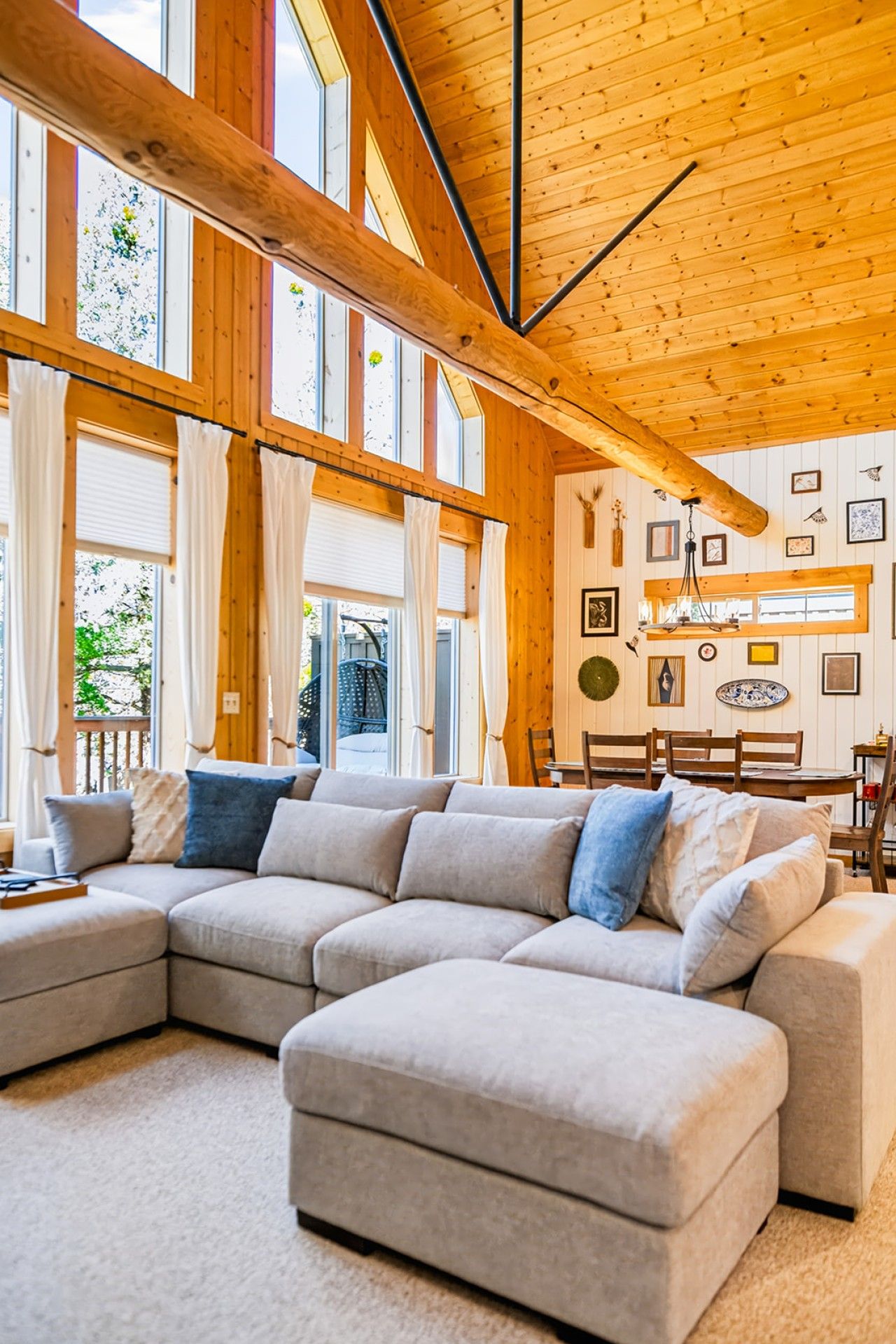 Ein modernes Wohnzimmer mit einer Eckcouch, großen Fenstern und einer Holzbalkendecke.