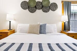 A hotel room with a large bed, two bedside tables with lamps, a decorative wall hanging, and a window with curtains.