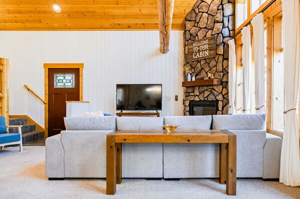A cabin interior with a stone fireplace, a television, a sofa, and a wooden table.