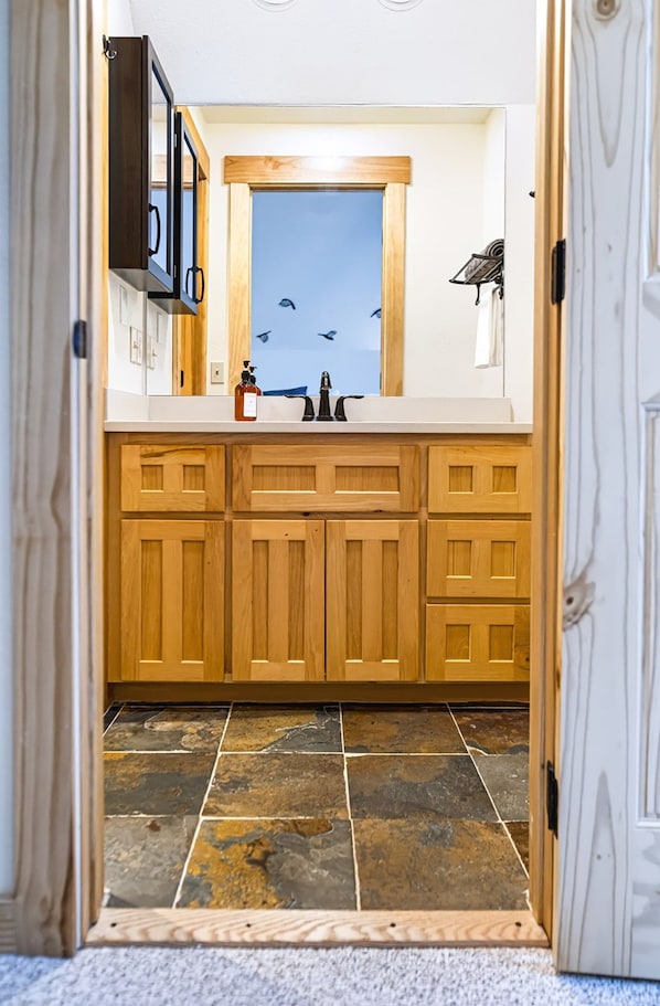 A kitchen with wooden cabinets, a stone tile floor, and a window with a view of the sky.