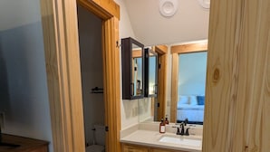 A bathroom with a wooden vanity, a mirror, a toilet, and a shower area. - Sage Creek Chalet At The Running Y (Klamath Falls)
