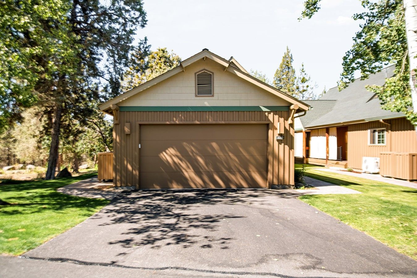 Un bâtiment d’un seul étage avec un garage, entouré d’arbres et d’une pelouse bien entretenue.