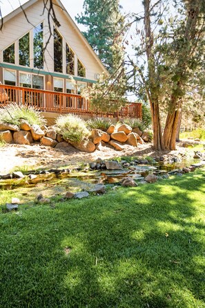 A house with a deck, a small stream, and a well-maintained lawn.