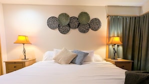 A hotel room with a large bed, two bedside tables with lamps, a decorative wall piece, and a view of the outside. - Sage Creek Chalet At The Running Y (Klamath Falls)