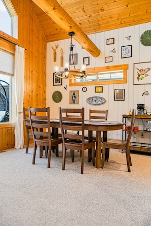 A dining area with a wooden table and chairs, a hanging light fixture, and wall-mounted decorations.