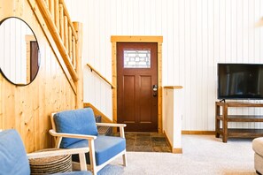 Un intérieur en bois avec un escalier, une porte dotée d’une fenêtre, un téléviseur posé sur un meuble et une chaise bleue.