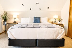 Une chambre avec un grand lit, deux tables de chevet avec des lampes, une plante en pot et des autocollants décoratifs représentant des oiseaux sur les murs.