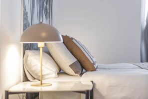 Ein ordentlich bezogenes Bett mit Kissen, einer Nachttischlampe und einer Wand mit vertikalem Muster.