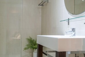 Un bagno moderno con un lavandino bianco, cabina doccia in vetro e una pianta in vaso.