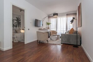 A modern living room with a sofa, armchair, and coffee table, a flat-screen TV mounted on the wall, and a large floor lamp. - CIty Central Flat in Madrid for 4 (Madrid)