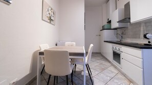 Una cuina compacta amb taula de dinar, cadires i electrodomèstics bàsics.