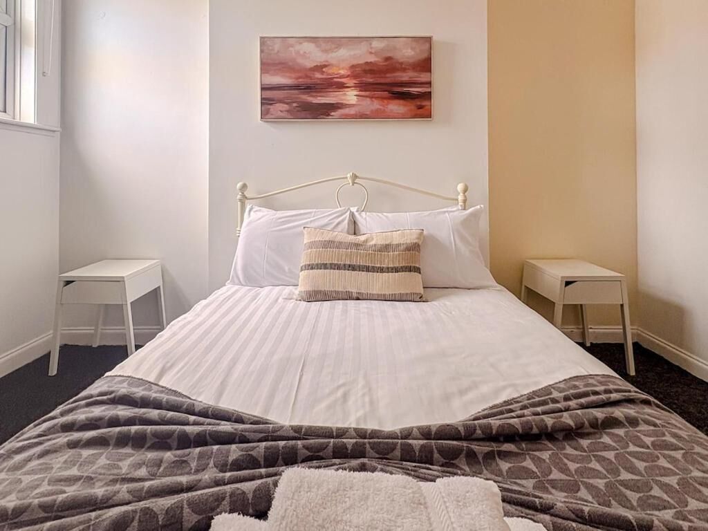 A neatly made bed with a patterned blanket, two bedside tables, and a wall-mounted painting.