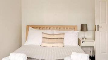 A neatly made bed with a wooden headboard, a bedside table with a lamp, and a door to the right.