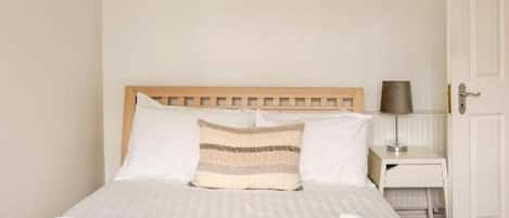 A neatly made bed with a wooden headboard, a bedside table with a lamp, and a door to the right.