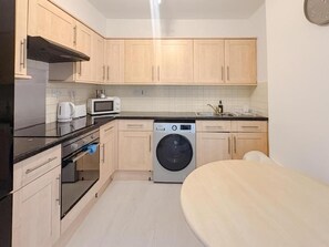 A compact kitchen with wooden cabinets, a microwave, a washing machine, and a dining area with a table.