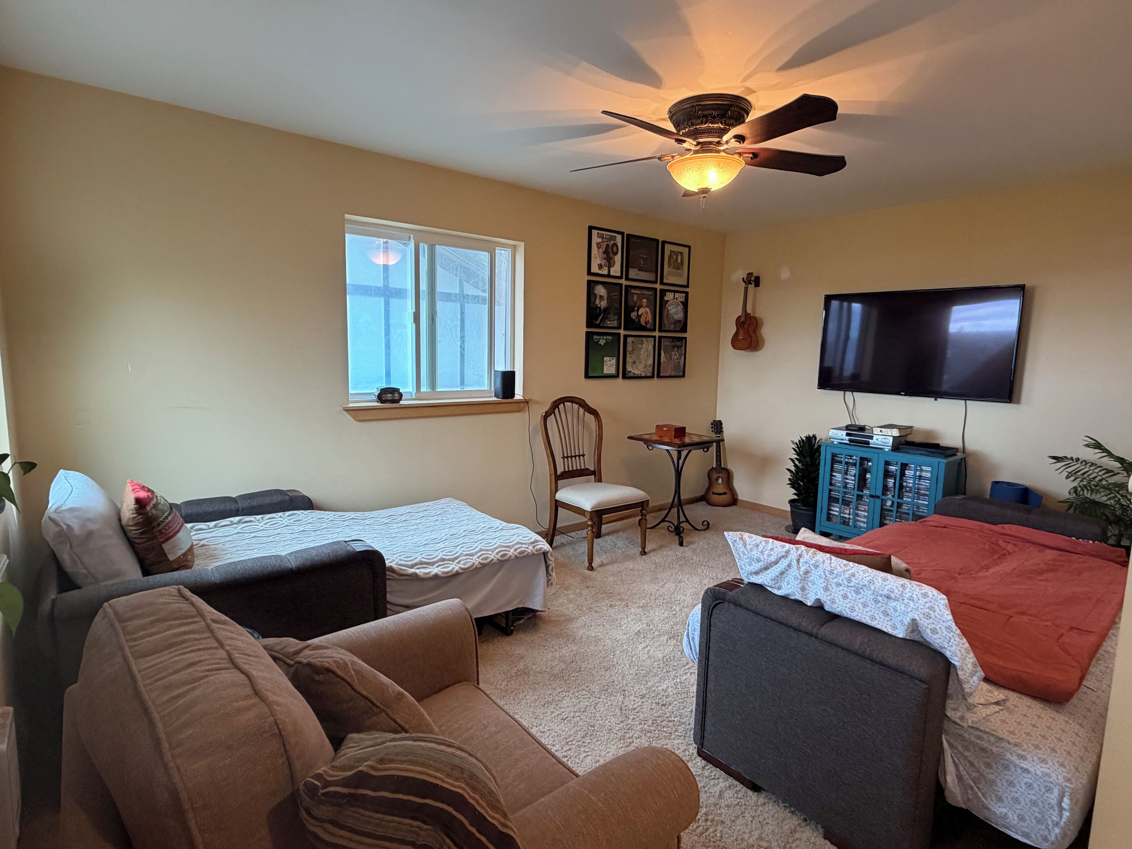 A living room with two sofas, a television, a ceiling fan, a window, and a guitar.
