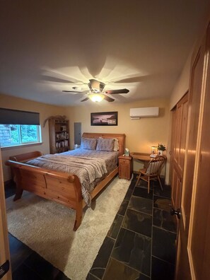 Une chambre à coucher avec un lit en bois, un ventilateur de plafond, une table de chevet, une chaise, un bureau et une fenêtre.