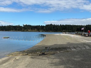 Une plage avec un sentier de galets menant à l’eau, une jetée et un mât sur lequel flotte un drapeau américain.