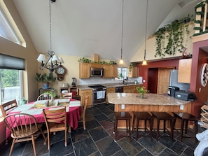 Une cuisine avec des meubles en bois, un îlot central doté d’un plan de travail en granit et un coin repas avec une nappe rouge.
