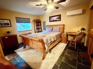 Une chambre à coucher avec un lit en bois, une table de chevet, une chaise, un bureau, une bibliothèque et un ventilateur de plafond.