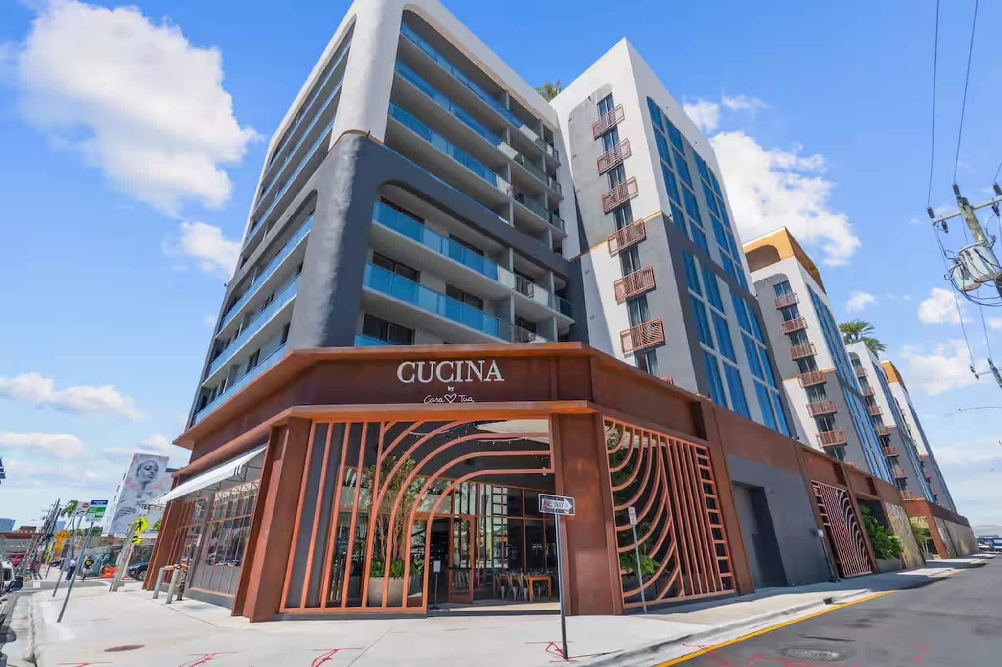 Ein mehrstöckiges Hotel mit modernem Design, das eine markante Eingangspartei mit der Aufschrift 'CUCINA by Coco & Tua' zeigt.