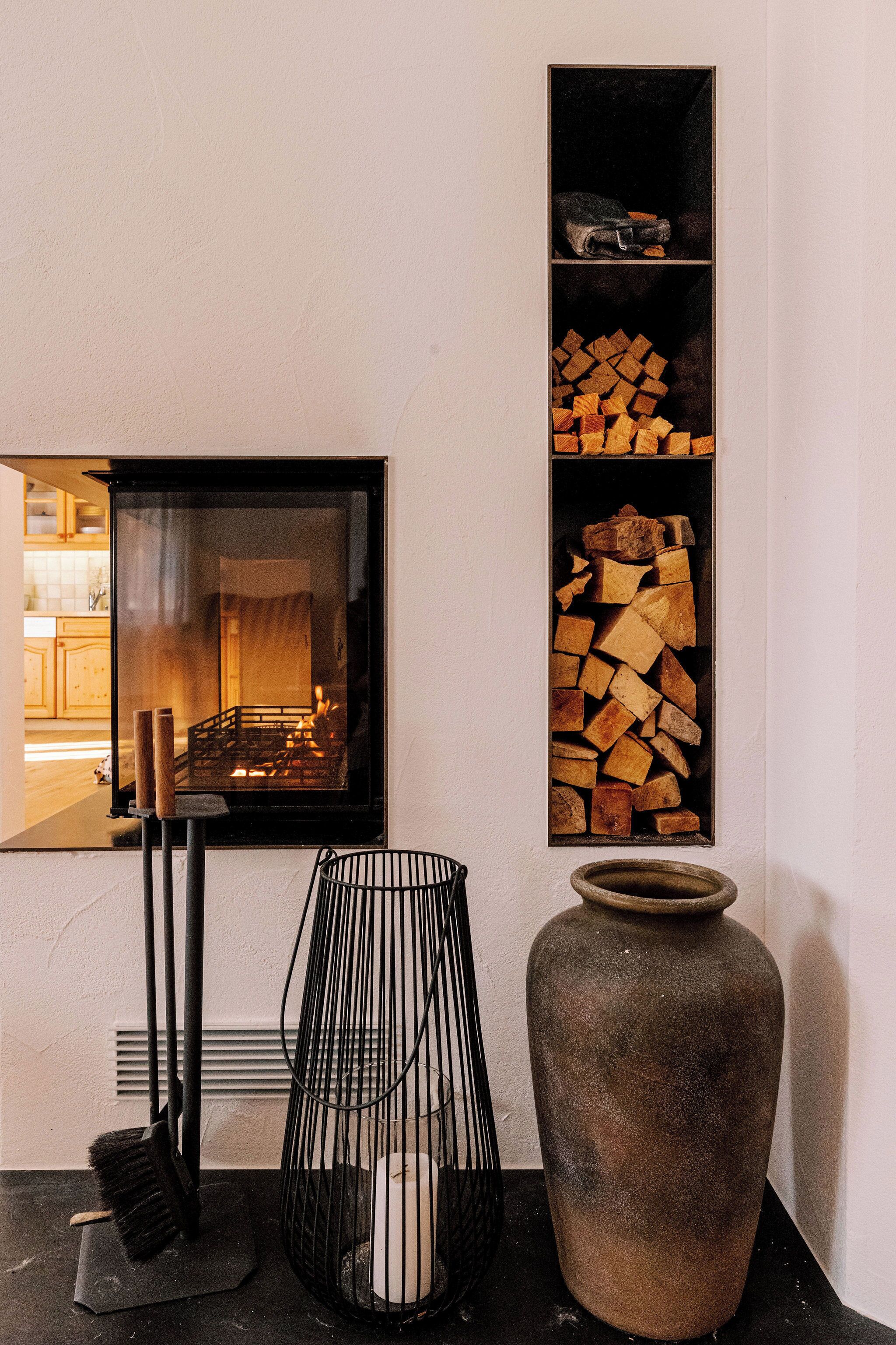 Ein Zimmer mit Kamin, einer großen Vase und einem Holzstoß.