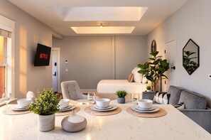 A modern living room with a dining area, a flat-screen TV mounted on the wall, a sofa, and a bed. - The Penn Hotel - Smart TV, AC & Downtown Location! (San Diego)