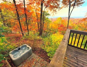 Een hottub op een houten terras met uitzicht op een bos in herfstkleuren.