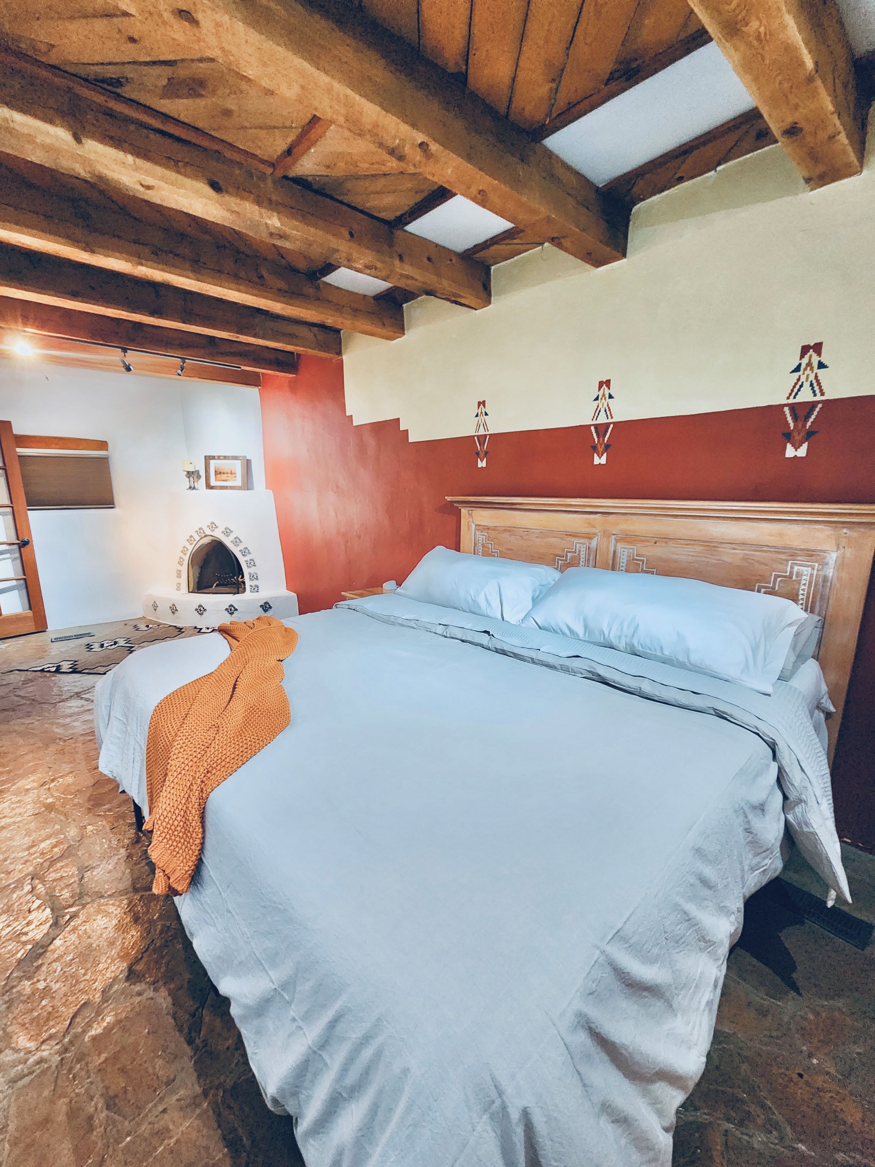 A bedroom with a bed, a fireplace, and wooden beams on the ceiling.