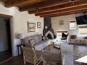 A cozy living room with a fireplace, a sofa, two wicker chairs, and a television mounted on the wall. - Gorgeous Adobe with Kivas & separate Casita, walk river path to Plaza, Patio (Santa Fe)