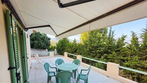 A covered outdoor patio with a table and chairs, surrounded by greenery.