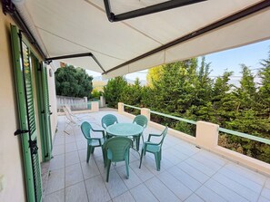 Une terrasse extérieure couverte, avec une table et des chaises, entourée de verdure.