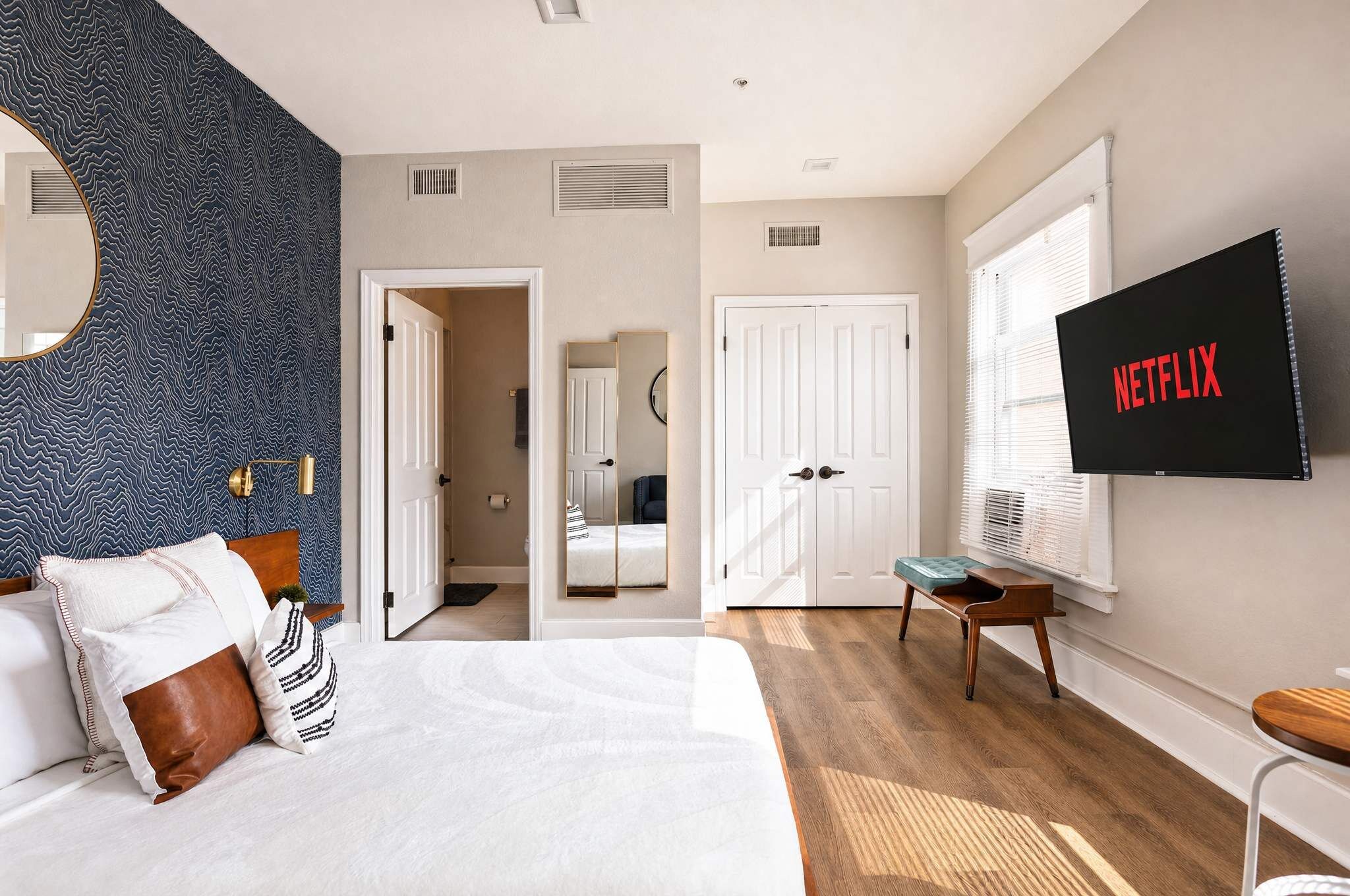 Un dormitorio moderno con una cama, un televisor montado en la pared y un espejo grande.