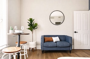A room with a blue sofa, a round mirror, a small table with glasses, and a potted plant. - The Penn Hotel - Queen Bed & Downtown Adventures!! (San Diego)