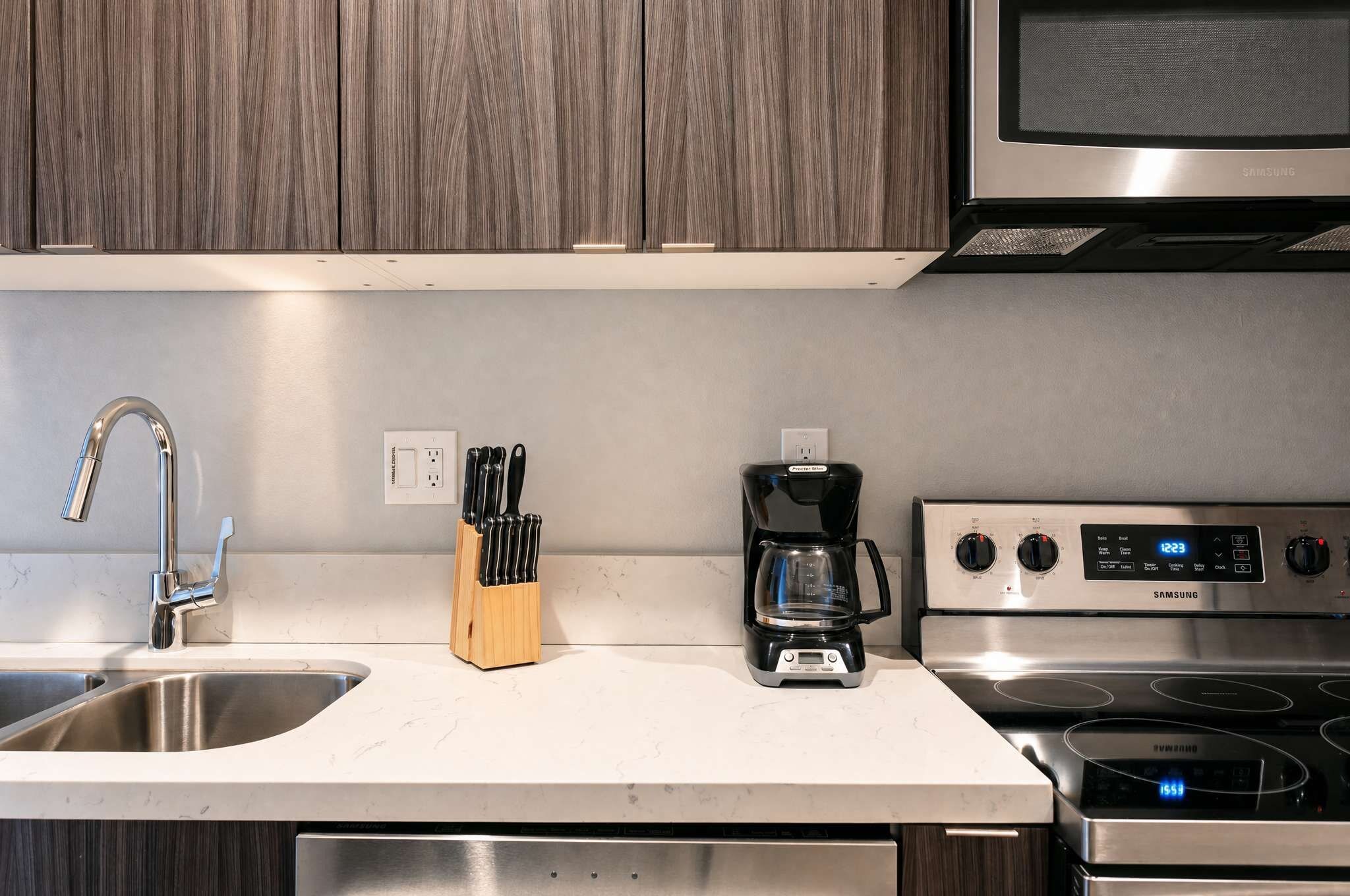 A kitchen with a stainless steel sink, a coffee maker, a stove, and wooden cabinets.