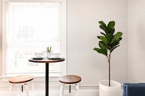 Una habitación con una mesa redonda, dos taburetes, una planta en maceta y una ventana con persianas.